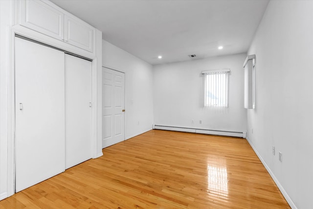 unfurnished bedroom with a closet, light hardwood / wood-style flooring, and baseboard heating