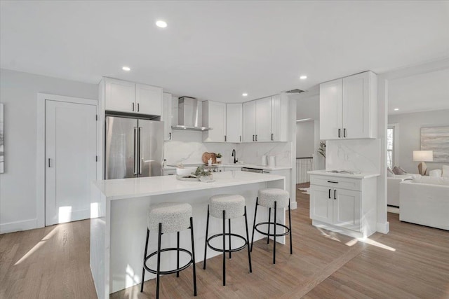 kitchen with backsplash, wall chimney range hood, white cabinets, and high end refrigerator