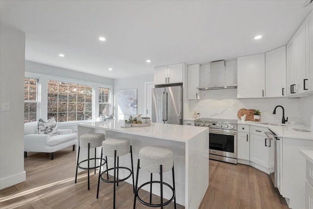 kitchen featuring a center island, sink, premium appliances, white cabinets, and wall chimney exhaust hood