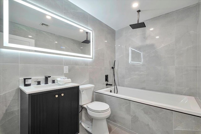 full bathroom with toilet, tiled shower / bath, tile walls, tile patterned floors, and vanity