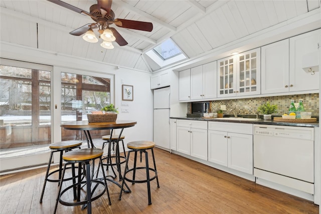 kitchen featuring lofted ceiling with skylight, light wood-type flooring, white cabinets, white appliances, and decorative backsplash