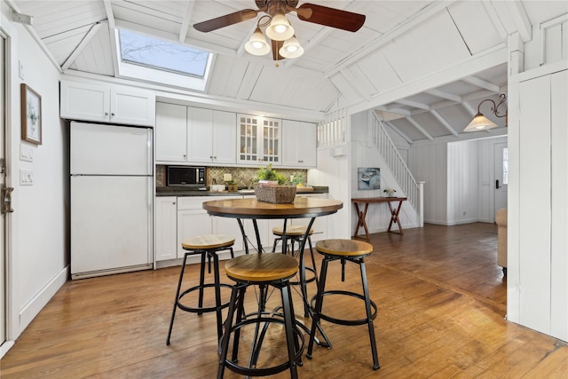 kitchen with white cabinets, white fridge, tasteful backsplash, and vaulted ceiling with skylight