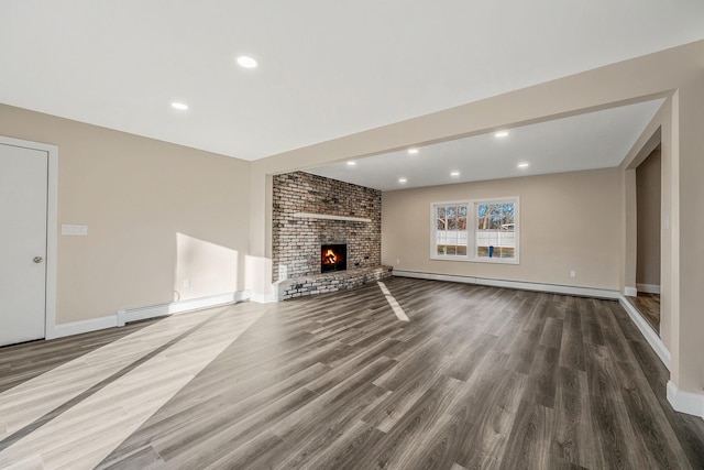 unfurnished living room featuring baseboard heating, dark hardwood / wood-style flooring, and a brick fireplace