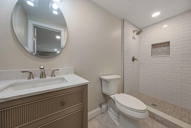 bathroom featuring tile patterned flooring, toilet, tiled shower, and vanity