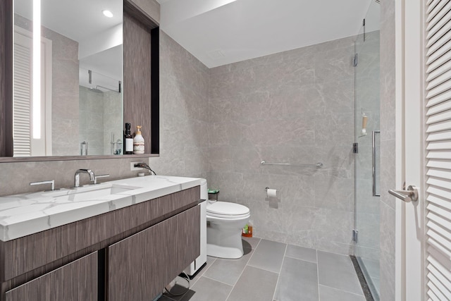 bathroom with tile walls, a shower with shower door, toilet, tile patterned floors, and vanity