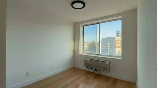 unfurnished room featuring a wall mounted AC, light wood-type flooring, and plenty of natural light