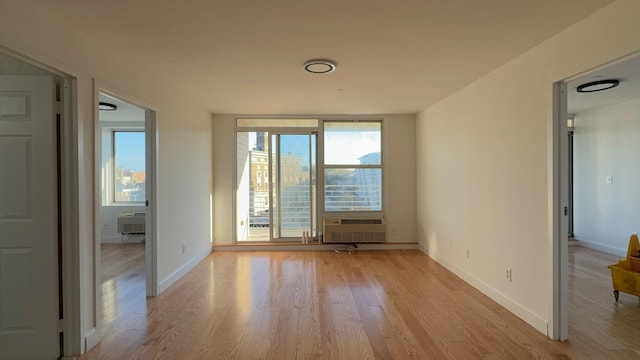 spare room with floor to ceiling windows, a wall unit AC, and light wood-type flooring