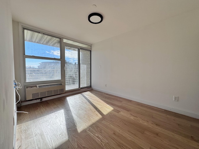 unfurnished room with floor to ceiling windows, a wall mounted AC, and light wood-type flooring