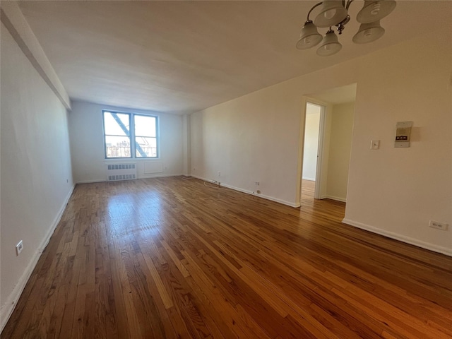 spare room with dark wood-type flooring, radiator heating unit, and a notable chandelier