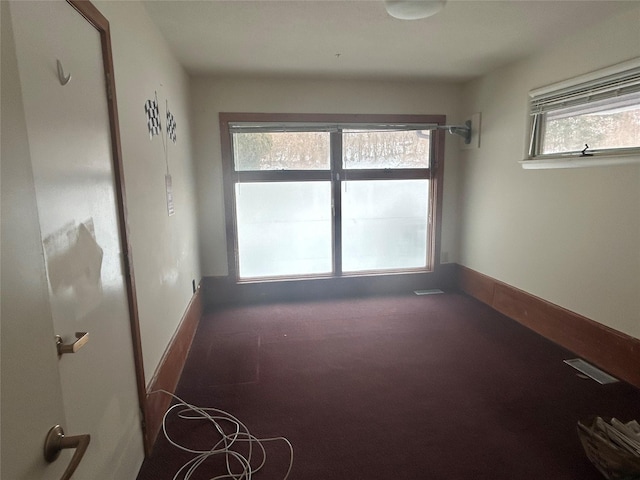 empty room featuring a wealth of natural light and dark colored carpet