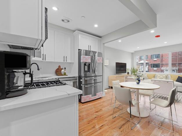 kitchen with light hardwood / wood-style floors, white cabinetry, light stone countertops, and stainless steel refrigerator with ice dispenser