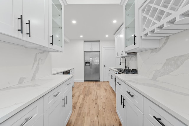 kitchen featuring white cabinetry, light wood-type flooring, light stone counters, and appliances with stainless steel finishes