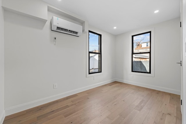 unfurnished room featuring a healthy amount of sunlight, light wood-type flooring, and a wall mounted AC