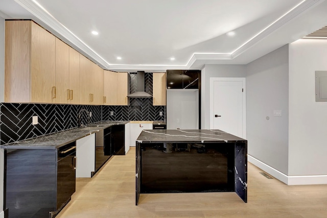 kitchen featuring a center island, wall chimney range hood, sink, light wood-type flooring, and light brown cabinetry