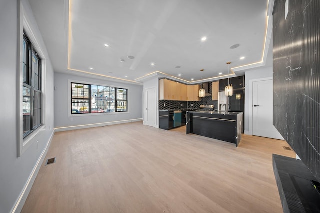 kitchen with pendant lighting, backsplash, a kitchen island with sink, light hardwood / wood-style floors, and light brown cabinets