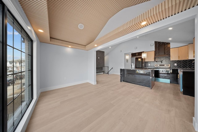 kitchen featuring vaulted ceiling, appliances with stainless steel finishes, wall chimney range hood, and light hardwood / wood-style flooring