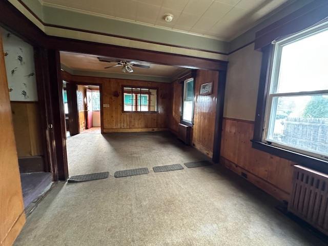 corridor with carpet, crown molding, wood walls, and radiator heating unit