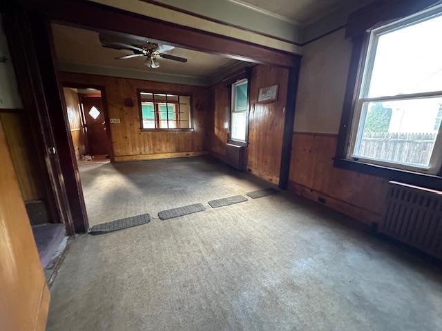 spare room featuring ceiling fan, carpet floors, wooden walls, crown molding, and radiator heating unit