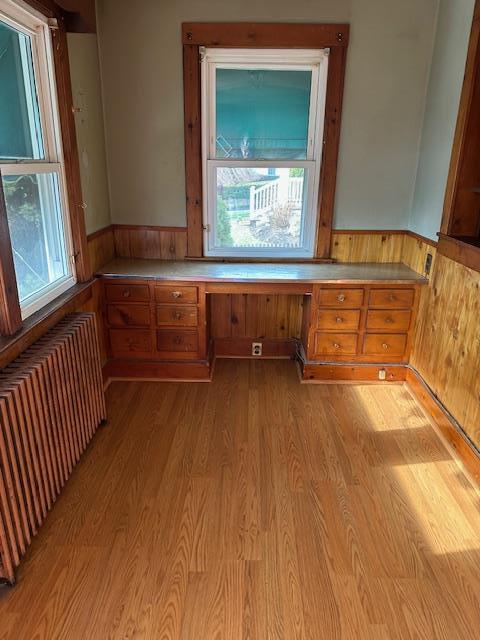 kitchen with radiator, wood walls, built in desk, and light wood-type flooring