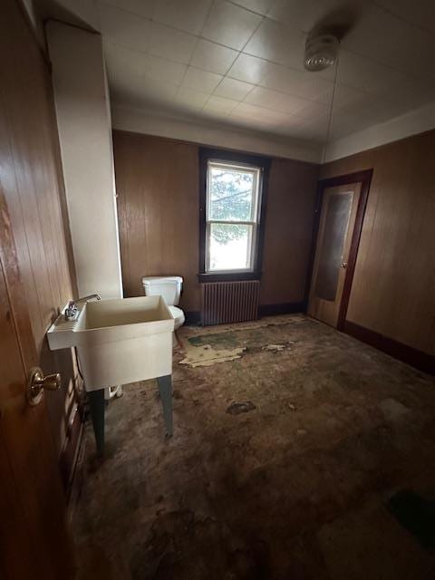 bathroom with radiator heating unit, toilet, and wood walls