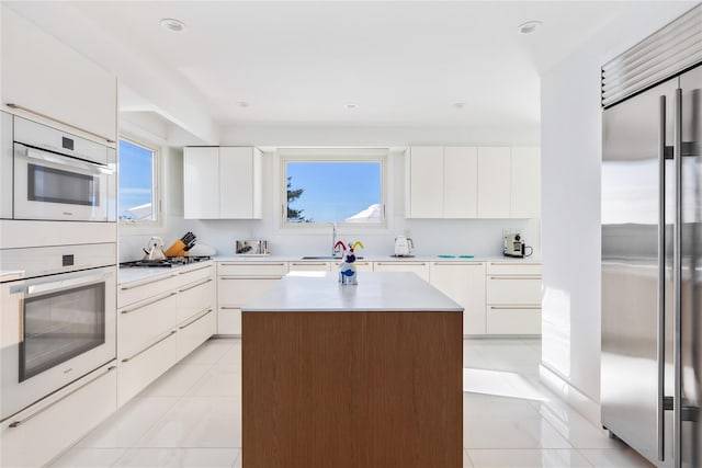 kitchen with white cabinetry, a center island, sink, stainless steel appliances, and light tile patterned floors