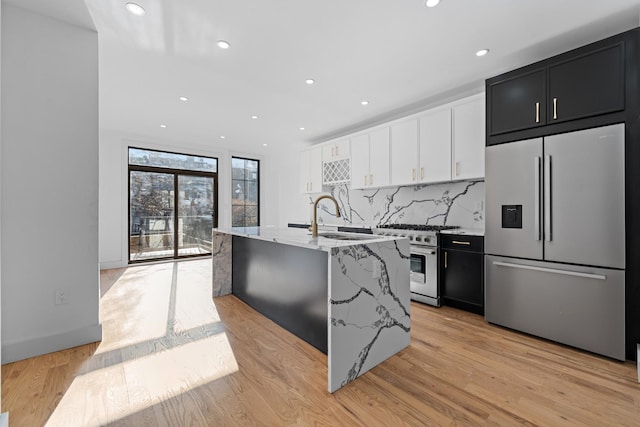 kitchen with light stone countertops, appliances with stainless steel finishes, sink, light hardwood / wood-style floors, and an island with sink