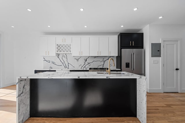 kitchen with a large island with sink, high end refrigerator, sink, and light stone countertops