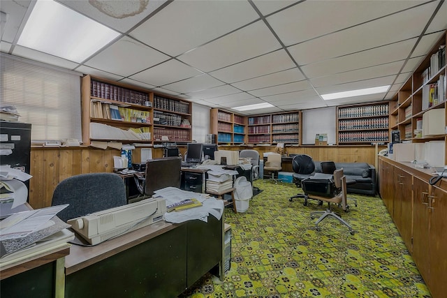 home office with a paneled ceiling, wooden walls, and carpet flooring