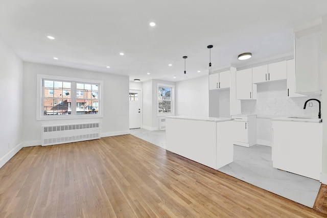 kitchen featuring sink, radiator heating unit, a center island, white cabinetry, and hanging light fixtures