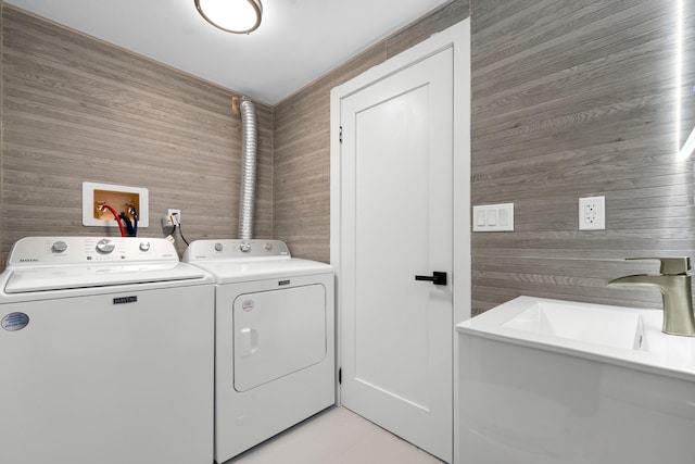 laundry area featuring light tile patterned flooring, washer and clothes dryer, wooden walls, and sink