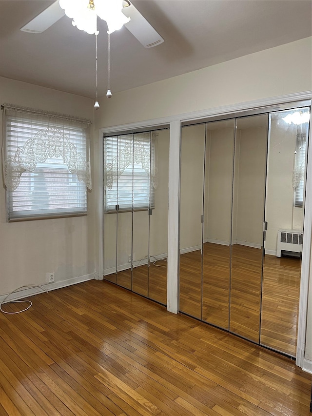 unfurnished bedroom featuring light wood-type flooring, ceiling fan, two closets, and radiator heating unit