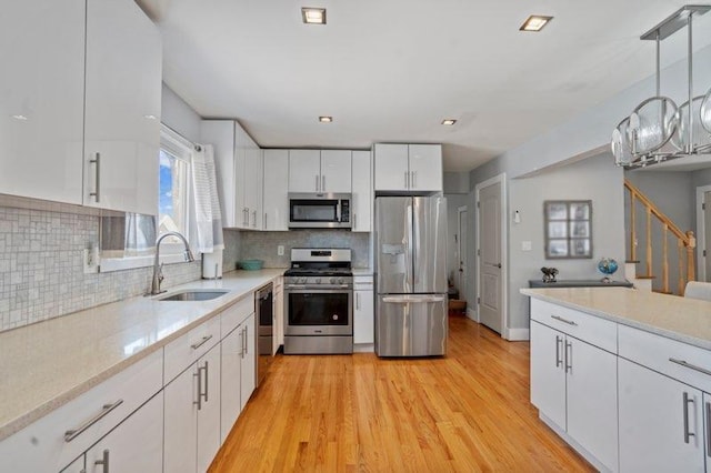 kitchen featuring appliances with stainless steel finishes, sink, white cabinets, hanging light fixtures, and light hardwood / wood-style flooring