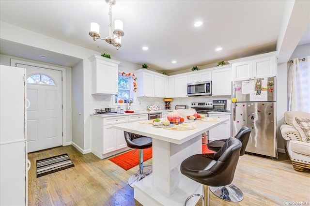 kitchen featuring a breakfast bar, light wood-type flooring, decorative light fixtures, white cabinetry, and stainless steel appliances