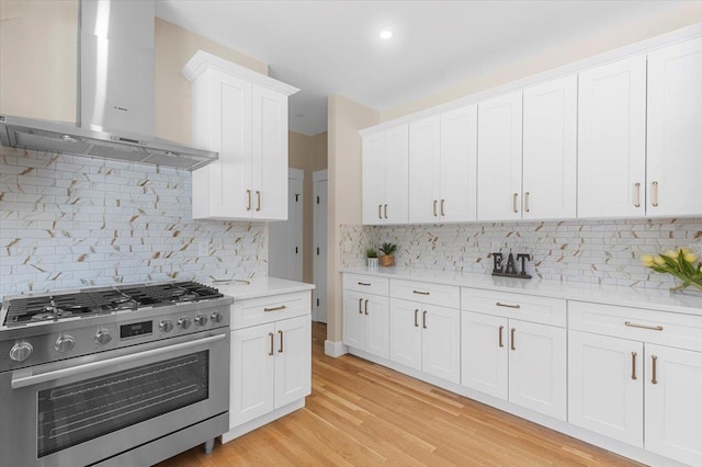 kitchen with wall chimney exhaust hood, white cabinetry, backsplash, and high end stainless steel range