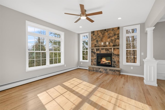 unfurnished living room with ornate columns, ceiling fan, a baseboard radiator, light hardwood / wood-style floors, and a stone fireplace