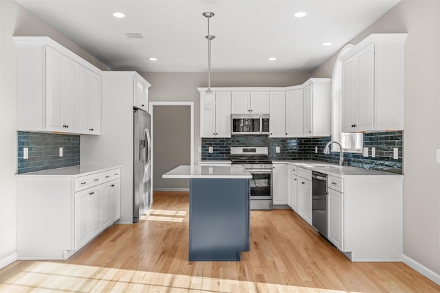 kitchen featuring light wood-type flooring, stainless steel appliances, white cabinets, a center island, and hanging light fixtures