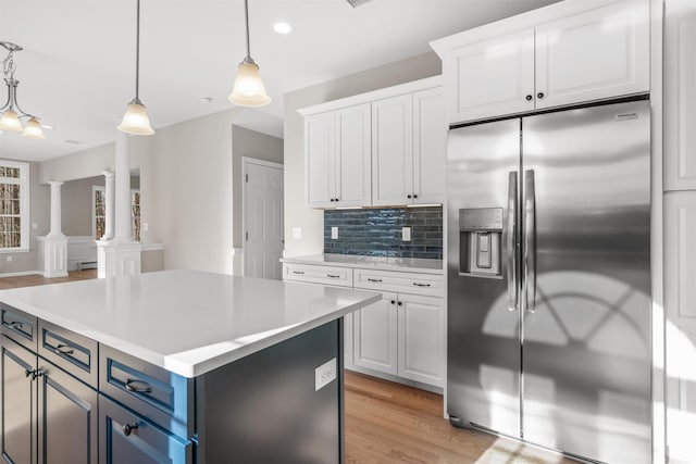 kitchen featuring stainless steel fridge, ornate columns, white cabinets, a kitchen island, and hanging light fixtures