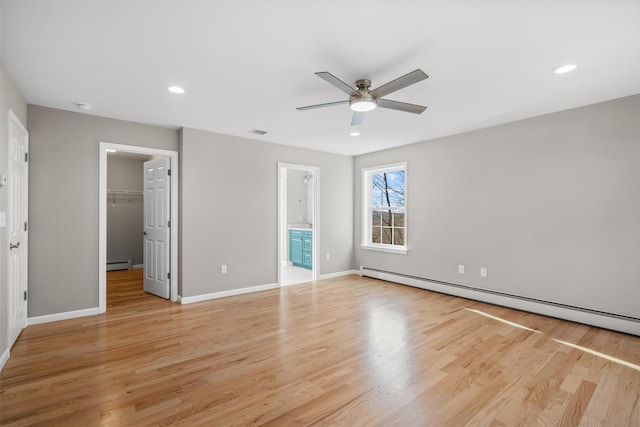 unfurnished bedroom with ensuite bath, ceiling fan, a spacious closet, light hardwood / wood-style flooring, and a baseboard heating unit