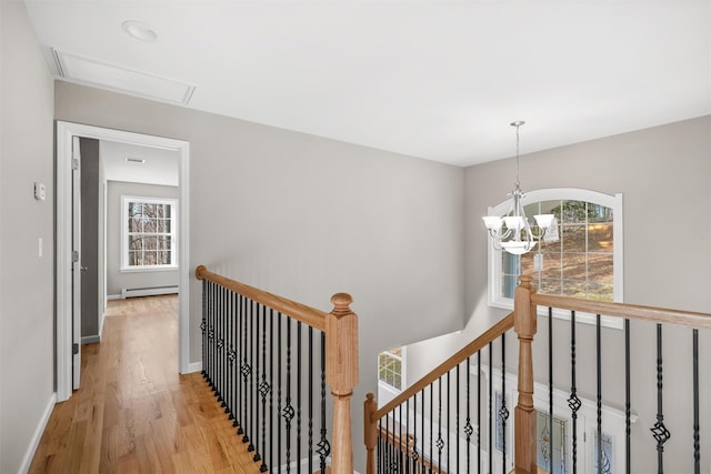 hallway with light hardwood / wood-style floors, a baseboard radiator, a wealth of natural light, and a chandelier