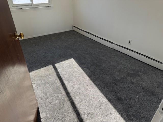 carpeted spare room featuring a baseboard radiator