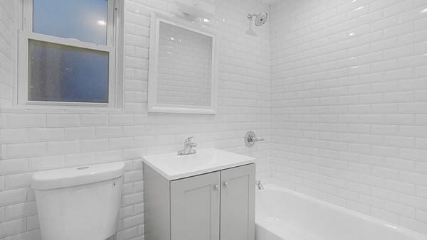 full bathroom featuring tiled shower / bath, vanity, toilet, and tile walls