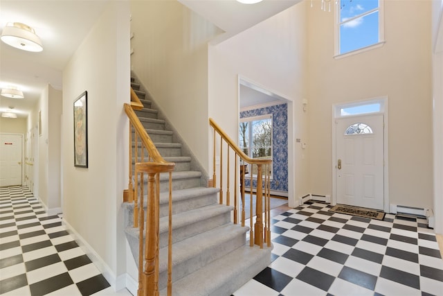 foyer entrance with a baseboard heating unit, baseboards, light floors, a towering ceiling, and stairs