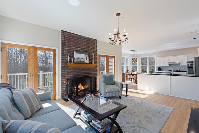 living room featuring french doors, a notable chandelier, a brick fireplace, and light wood finished floors