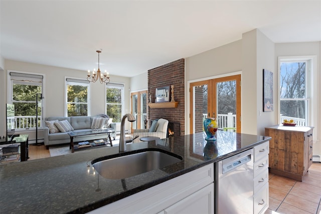 kitchen featuring open floor plan, dishwasher, dark stone counters, white cabinetry, and a sink