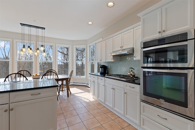 kitchen with light tile patterned floors, appliances with stainless steel finishes, under cabinet range hood, dark countertops, and backsplash