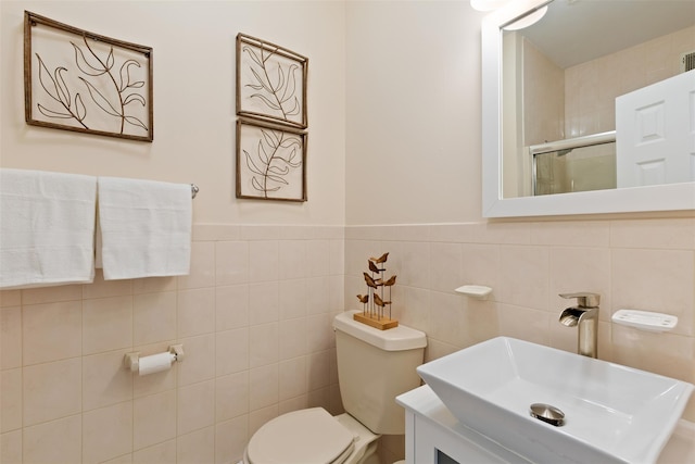 bathroom with a shower stall, tile walls, a wainscoted wall, toilet, and vanity