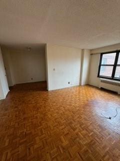 unfurnished room featuring radiator heating unit, a textured ceiling, and parquet floors