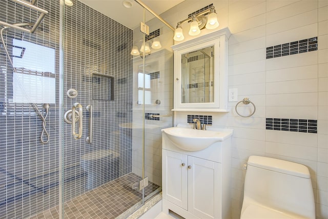 bathroom featuring tile walls, vanity, a shower with shower door, and toilet