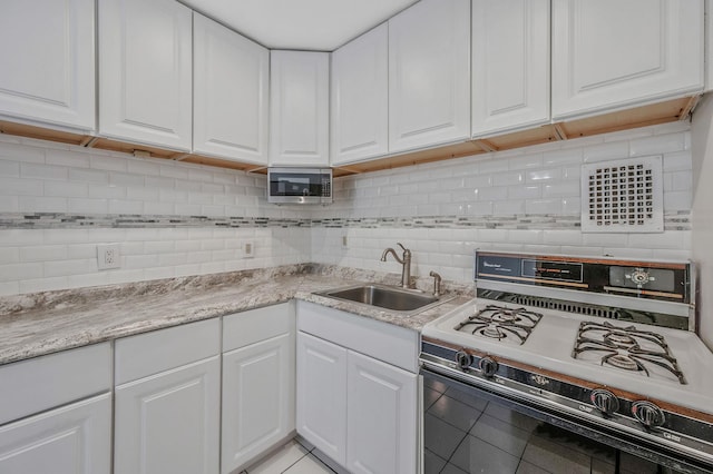 kitchen with white gas range, sink, decorative backsplash, and white cabinets