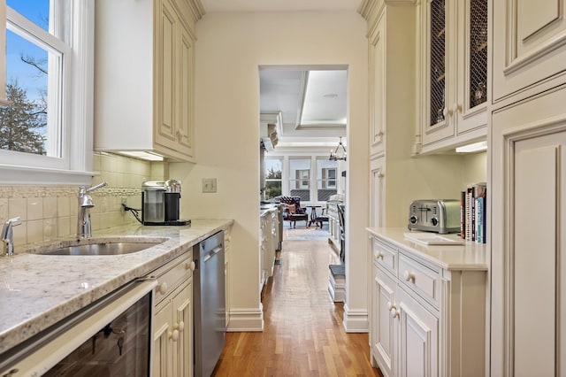 kitchen with stainless steel dishwasher, a healthy amount of sunlight, cream cabinetry, and light stone countertops